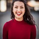 Woman with long dark hair wearing a red sweater smiling at camera