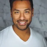 Professional headshot of a smiling man with dark hair wearing a white v-neck shirt