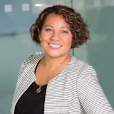 Professional headshot of woman with curly brown hair wearing striped cardigan
