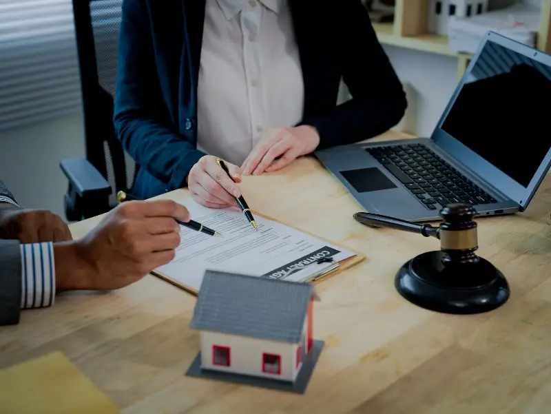 Two professionals reviewing legal documents at desk with gavel and house model