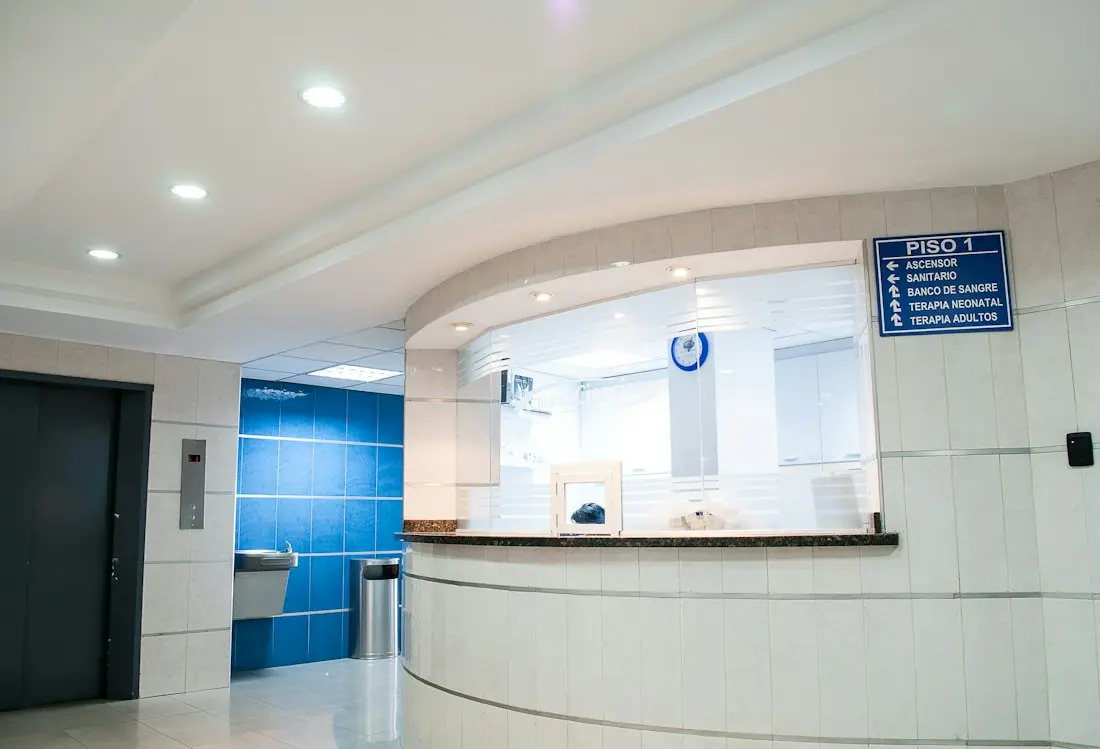 Modern hospital reception desk with blue tile accents and floor-to-ceiling windows on first floor