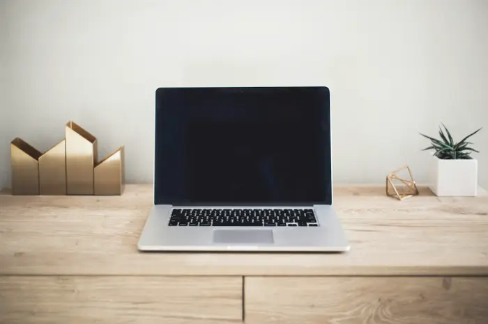 Laptop with black screen on wooden desk with desk organizer, succulent plant, and geometric gold decoration